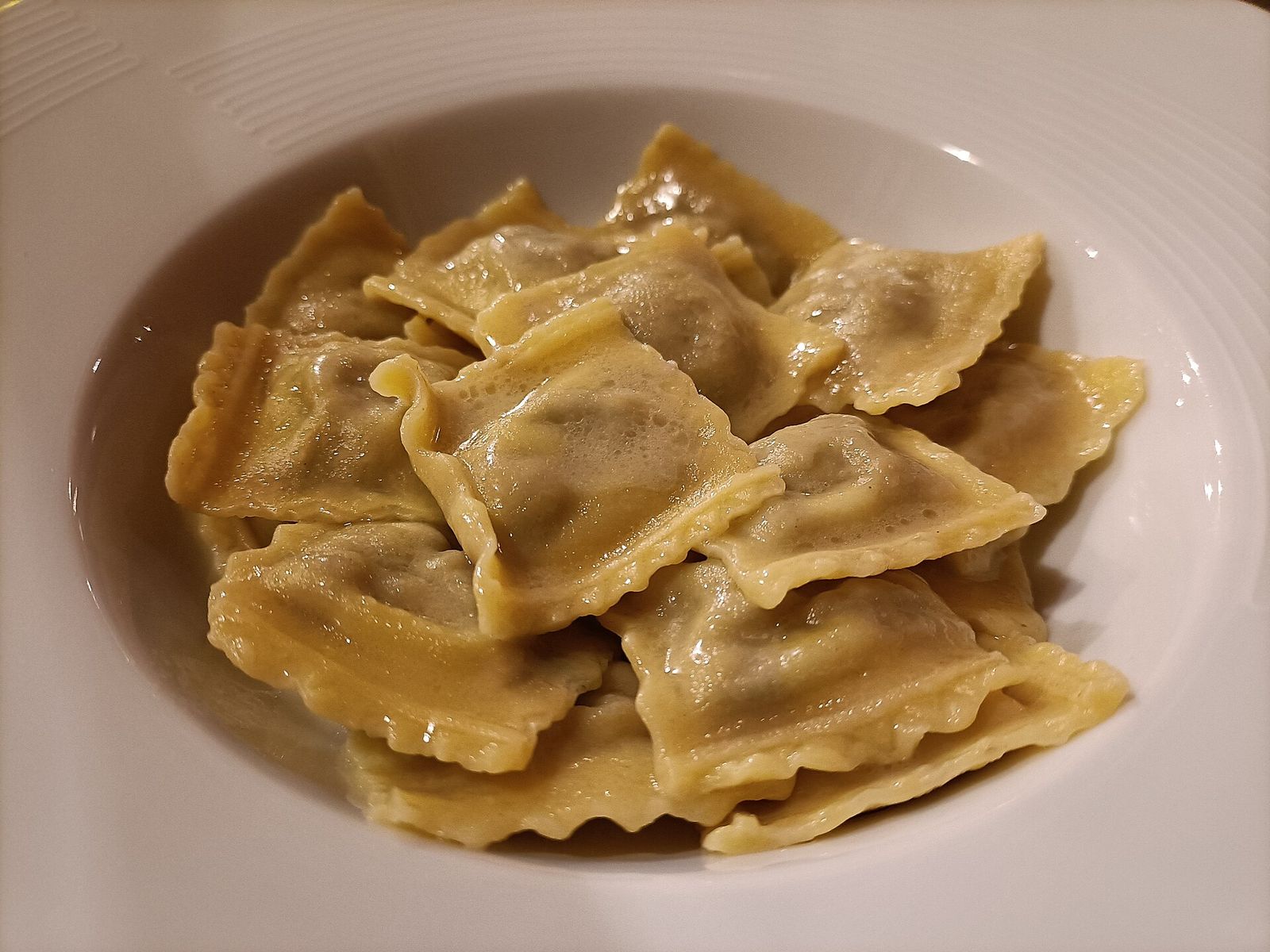 Un piatto fondo di agnolotti piemontesi di forma quadrata, appena conditi